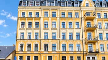 Ein mehrstöckiges Gebäude mit gelber Fassade, zahlreichen Fenstern und einem Hauseingang an der Ecke.
