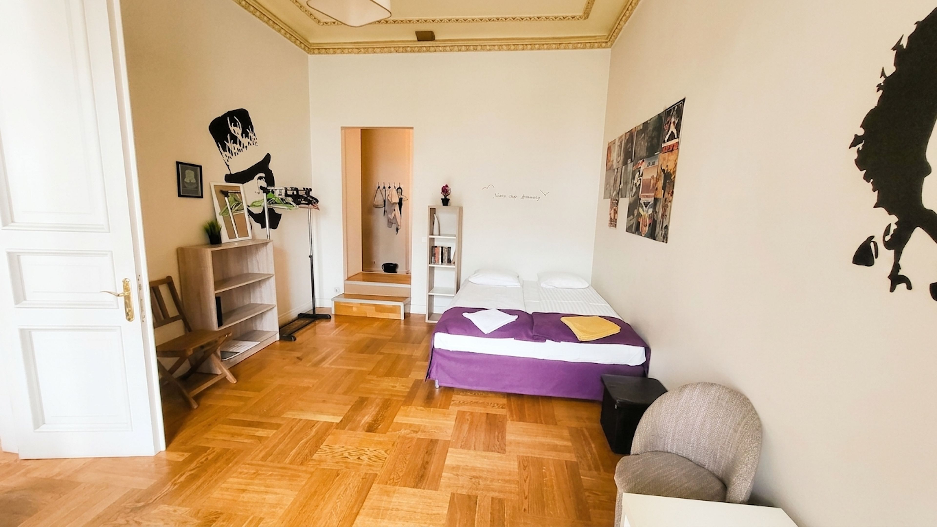 A room with a bed, a chair, a wardrobe, and a shelf with various items.