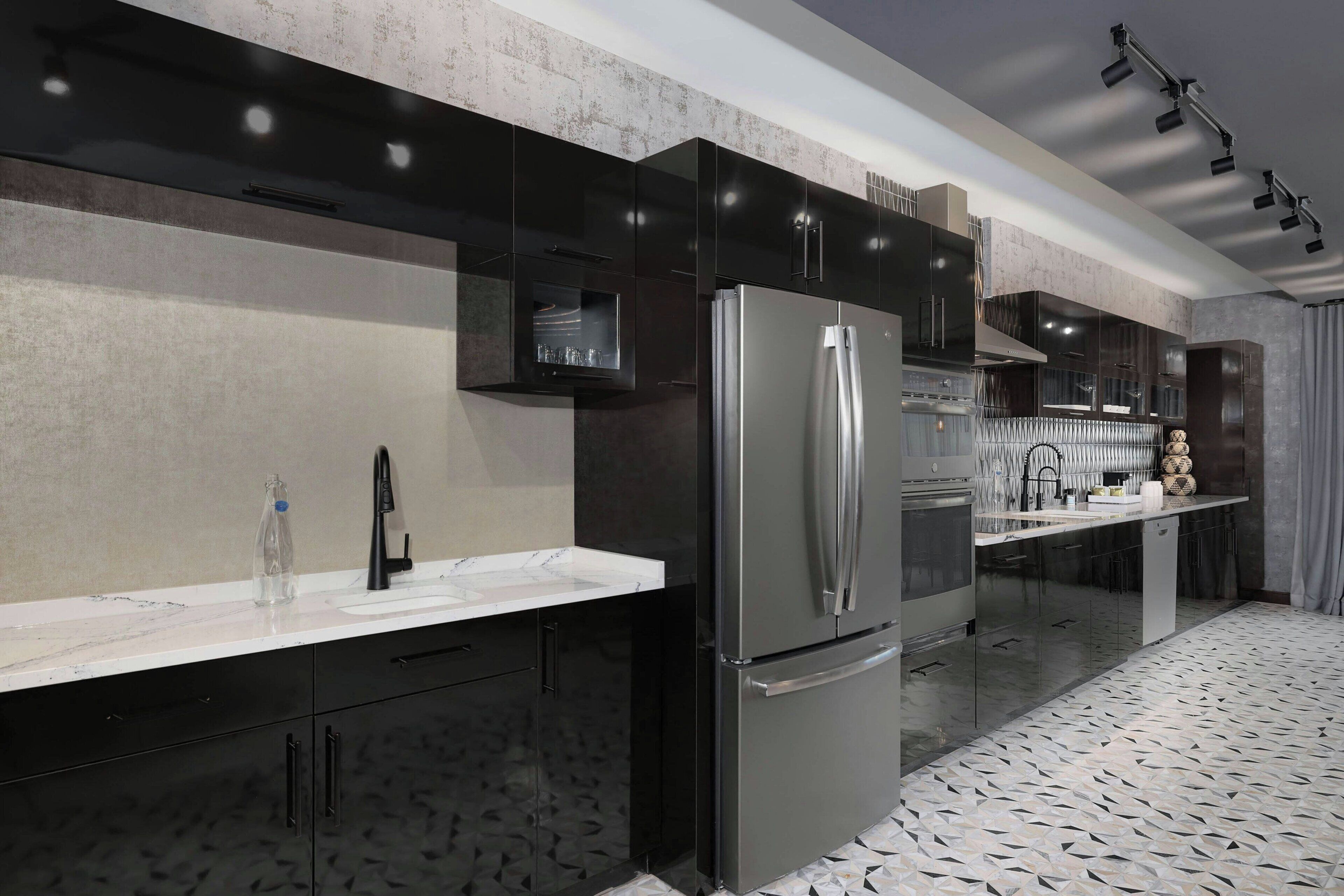 A modern kitchen with a stainless steel refrigerator, black cabinets, and a marble countertop.