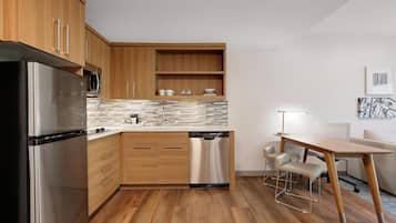 A compact kitchen with wooden cabinets, a stainless steel refrigerator, a dishwasher, and a tiled backsplash.
