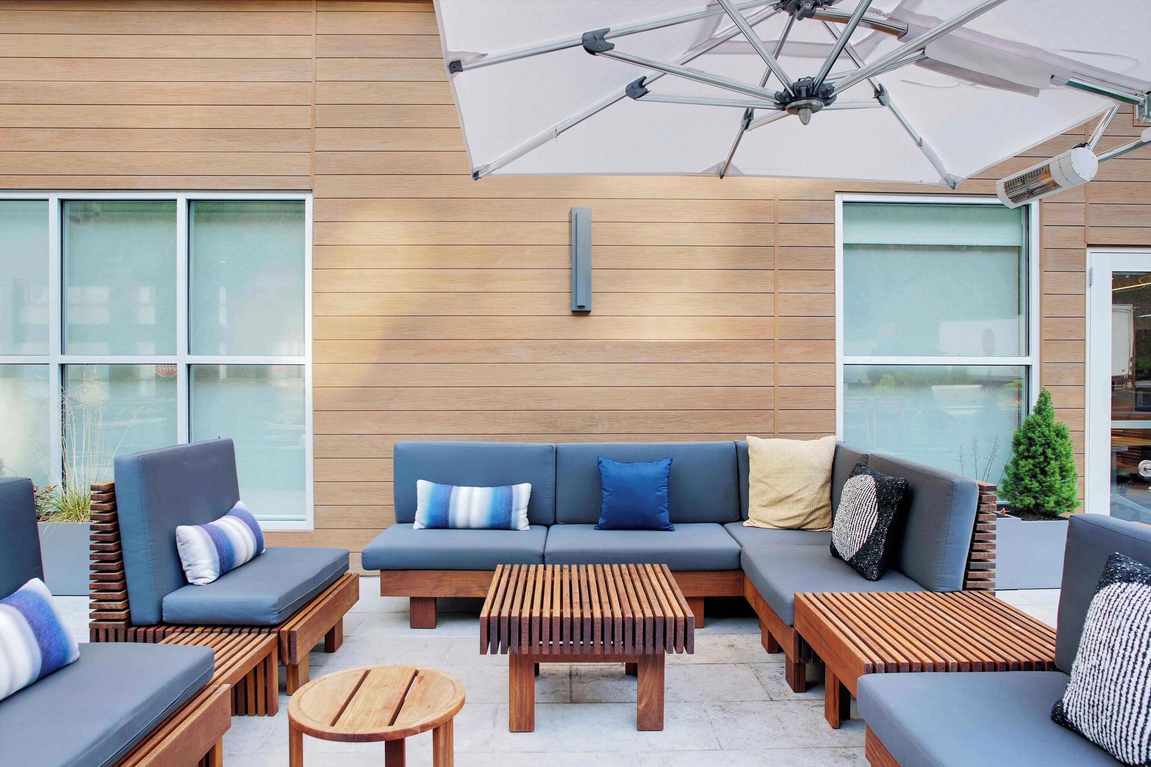 An outdoor seating area with a wooden wall, a blue sofa with cushions, and a wooden table.