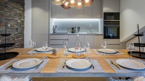 A modern dining area with a wooden table set for six, a stone wall, and a kitchen in the background. - Bright apartment for 6 in Méribel with fireplace (Méribel)