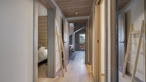 A hallway with wooden flooring, a bed in the left room, and a view of a balcony with a wooden railing. - Bright apartment for 6 in Méribel with fireplace (Méribel)