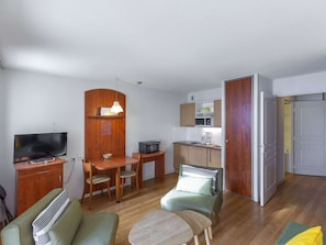 Um espaço de estar compacto com cozinha compacta, área de jantar, sala de estar com sofá e poltrona, e televisão.