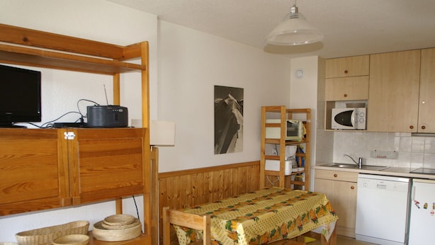 A compact kitchen with wooden furniture, a dining table, and a microwave.