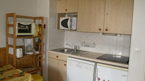 A compact kitchen with wooden cabinets, a microwave, a sink, and a dishwasher.