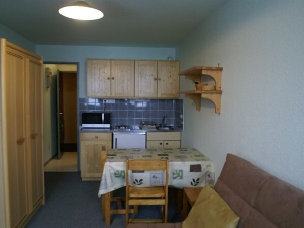 A compact kitchen with wooden cabinets, a microwave, and a sink. There is a dining table with chairs and a brown sofa. - Studio 18m² for 3, near slopes, pets allowed (Le Pleynet)