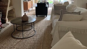 En rummelig stue med en stor sofa, et sofabord og en pejs. Store vinduer giver udsigt til en have.