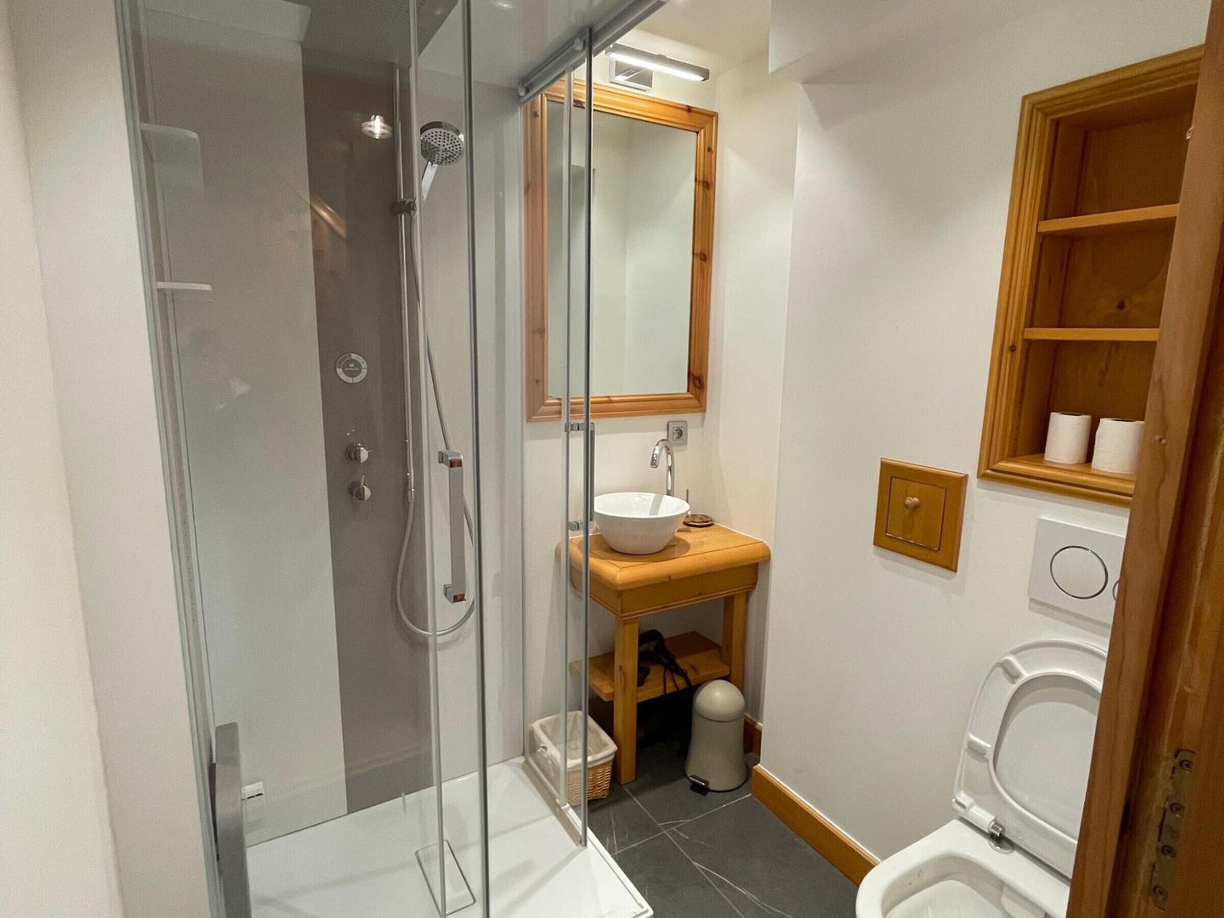 Een moderne badkamer met een douchecabine van glas, een houten wastafelmeubel met een wastafel en een toilet.