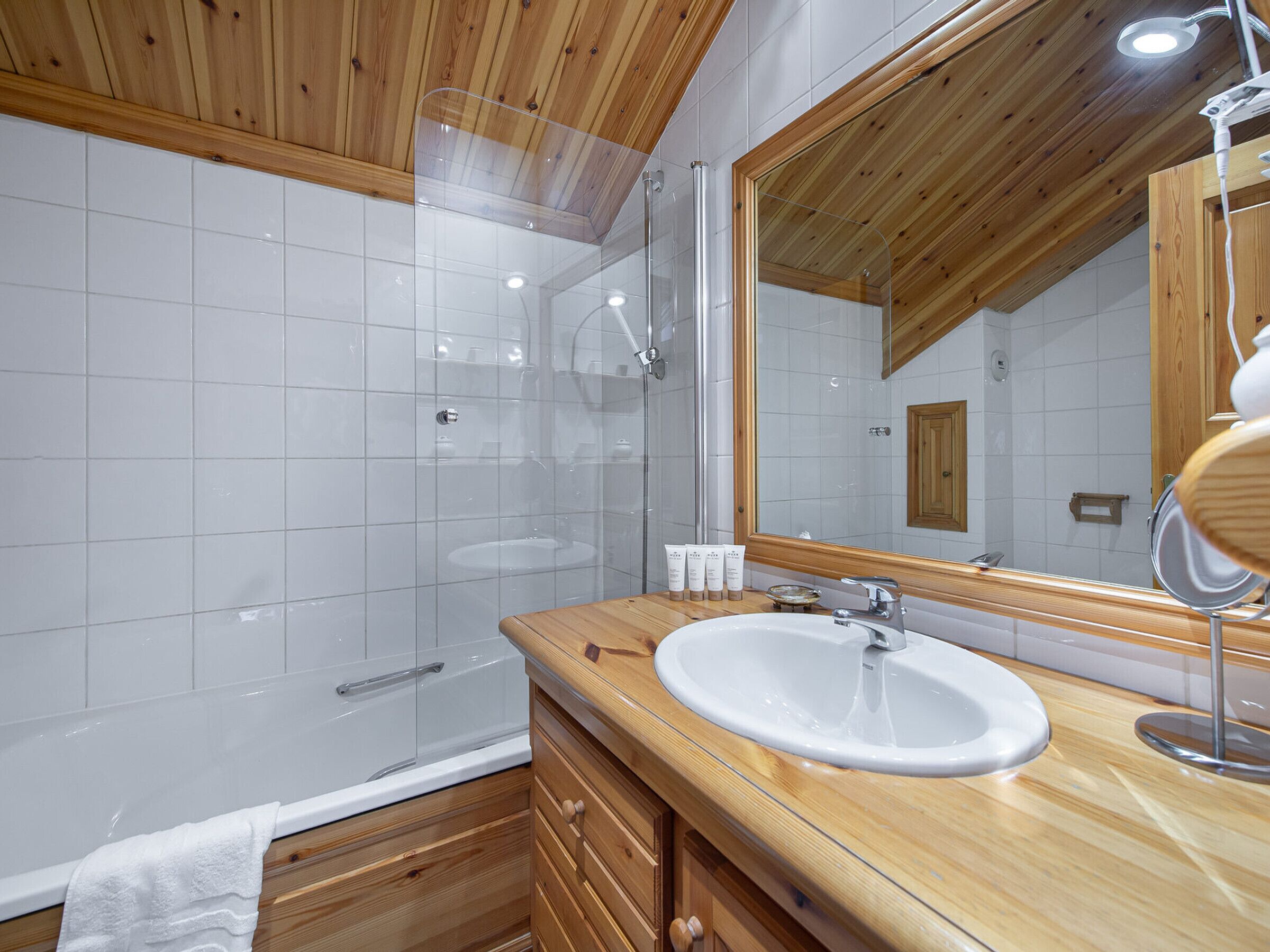 Un baño moderno con tocador de madera, un lavabo blanco, un espejo grande y una ducha con paredes de vidrio.