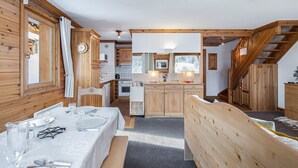 A cozy wooden cabin interior with a dining area, kitchen, and a staircase leading to a loft.