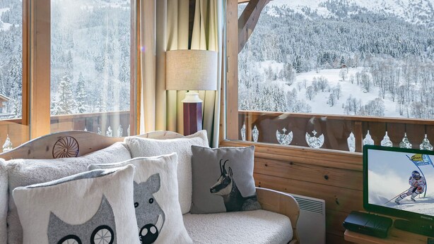 A cozy cabin room with a wooden interior, a sofa with animal-themed cushions, a lamp, and a television displaying a skier.