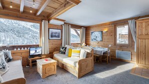 A cozy cabin with wooden walls, a sofa, a dining table, and a TV.