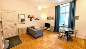 Una sala de estar con sofá, televisión, mesa de comedor, sillas y ventana con cortinas.