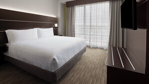 A hotel room with a large bed, a flat-screen TV, a window with curtains, and a carpeted floor. - Holiday Inn Express & Suites Woodside LaGuardia Airport by IHG (Woodside)