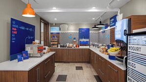 A modern breakfast area with a self-serve station, bakery section, and a refrigerator stocked with yogurt, eggs, and milk. - Holiday Inn Express & Suites Woodside LaGuardia Airport by IHG (Woodside)