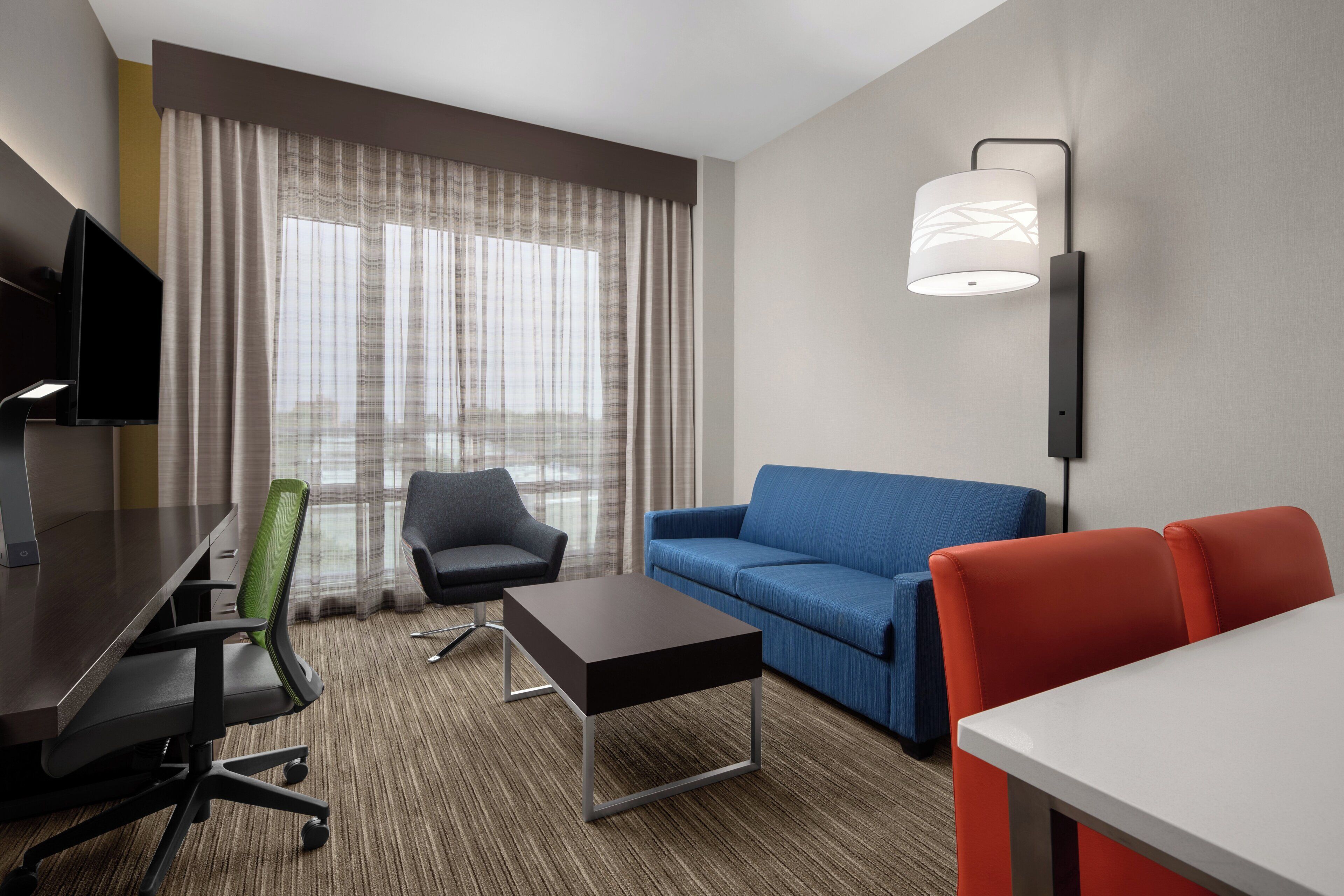 Una habitación de hotel con escritorio, dos sillas, sofá, mesa de centro y televisor.