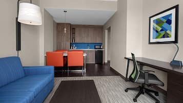 A modern living room with a blue sofa, a dining area with orange chairs, a kitchen with wooden cabinets, and a desk with a chair.