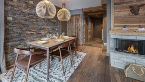 A dining area with a stone wall, wooden table, chairs, and pendant lights. - New apartment in Méribel with parking, for 6 people (Méribel)
