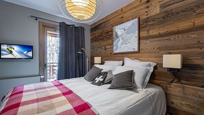 A bedroom with a large bed, a mounted TV, a wooden wall, and a window with curtains. - New apartment in Méribel with parking, for 6 people (Méribel)