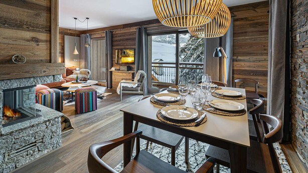 A cozy, rustic interior with a stone fireplace, wooden walls, and a dining area set for a meal. - New apartment in Méribel with parking, for 6 people (Méribel)