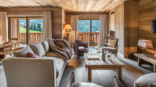 A cozy log cabin interior with a sofa, chairs, a table, and a balcony with a scenic view. - Ski-In Ski-Out Apartment with Spa Access and Mountain Views in Méribel (Méribel)