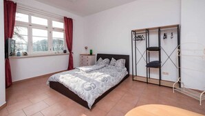 A bedroom with a bed, a wardrobe, a window with curtains, and a small table.