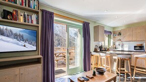 Ein gemütliches Wohnzimmer mit einem großen Flachbildfernseher, Holzmöbeln, einer Essecke und einer Küche mit Holzausstattung.