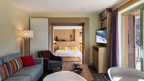 Ein modernes Hotelzimmer mit Sofa, Sesseln und einem Bett mit einem Holz-Kopfteil.
