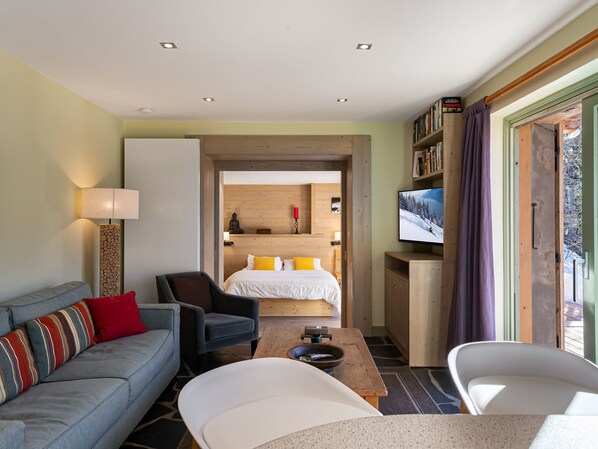 A modern hotel room with a sofa, armchair, and a bed with a wooden headboard. - Quiet apartment with terrace and parking, close to slopes (Méribel)
