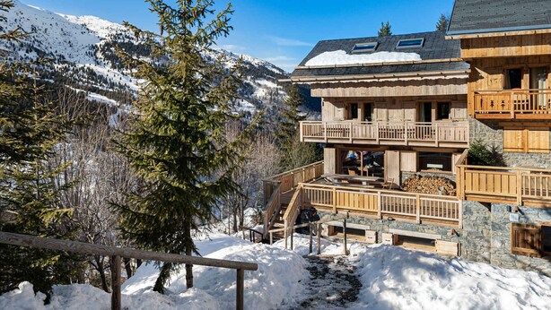 Eine Holzhütte mit Balkon, umgeben von schneebedeckten Bergen und Bäumen.