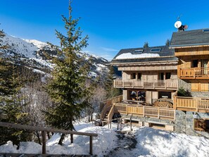 A wooden chalet with a balcony, surrounded by snow-covered mountains and trees. - Quiet apartment with terrace and parking, close to slopes (Méribel)