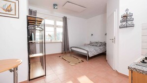 A compact bedroom with a bed, a small table, a wardrobe, and a window with curtains. - Landhaus Karnin - Vacation at the Peenestrom - FEWO3 (Usedom OT Karnin)