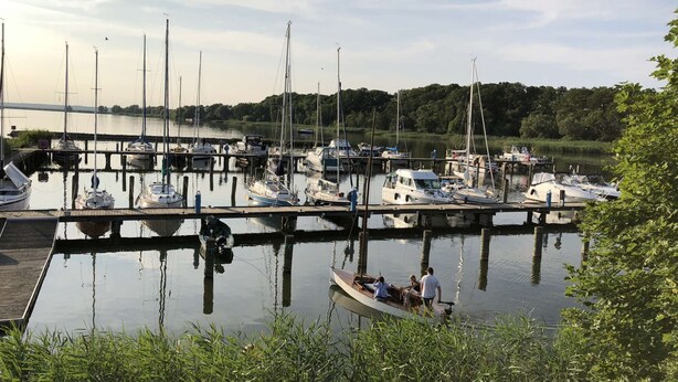 A marina with various boats docked at wooden piers, surrounded by greenery and a distant bridge. - Landhaus Karnin - Vacation at the Peenestrom - FEWO3 (Usedom OT Karnin)