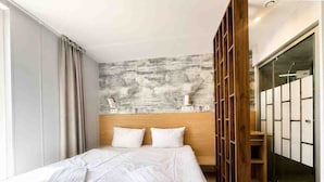 Moderni hotellihuone, jossa on suuri sänky, puinen pääty, liukuovilla varustettu vaatekaappi ja näkymä kaupunkiin.