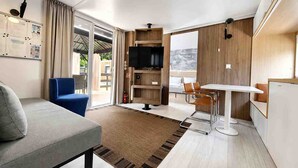 Moderni hotellihuone, jossa on sohva, ruokapöytä tuoleineen, taulutelevisio ja suuri ikkuna, josta avautuu näkymä.