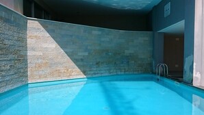 En swimmingpool med klart, blåt vand, omgivet af stenvægge og en metalstige.
