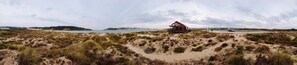 Eine Strandhütte mit rotem Dach und Holzbau, umgeben von Dünen und einer Küstenlandschaft.