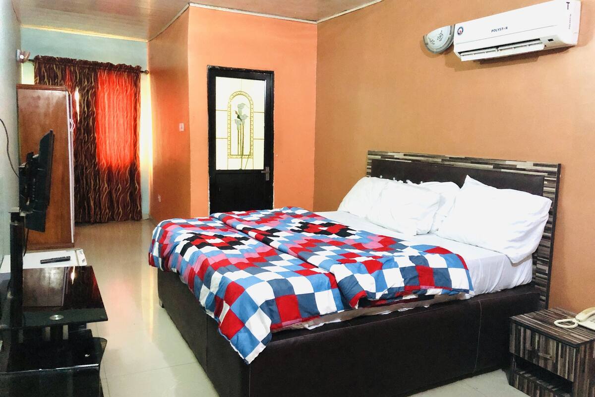 A hotel room with a bed, a TV, an air conditioner, and a door with curtains.