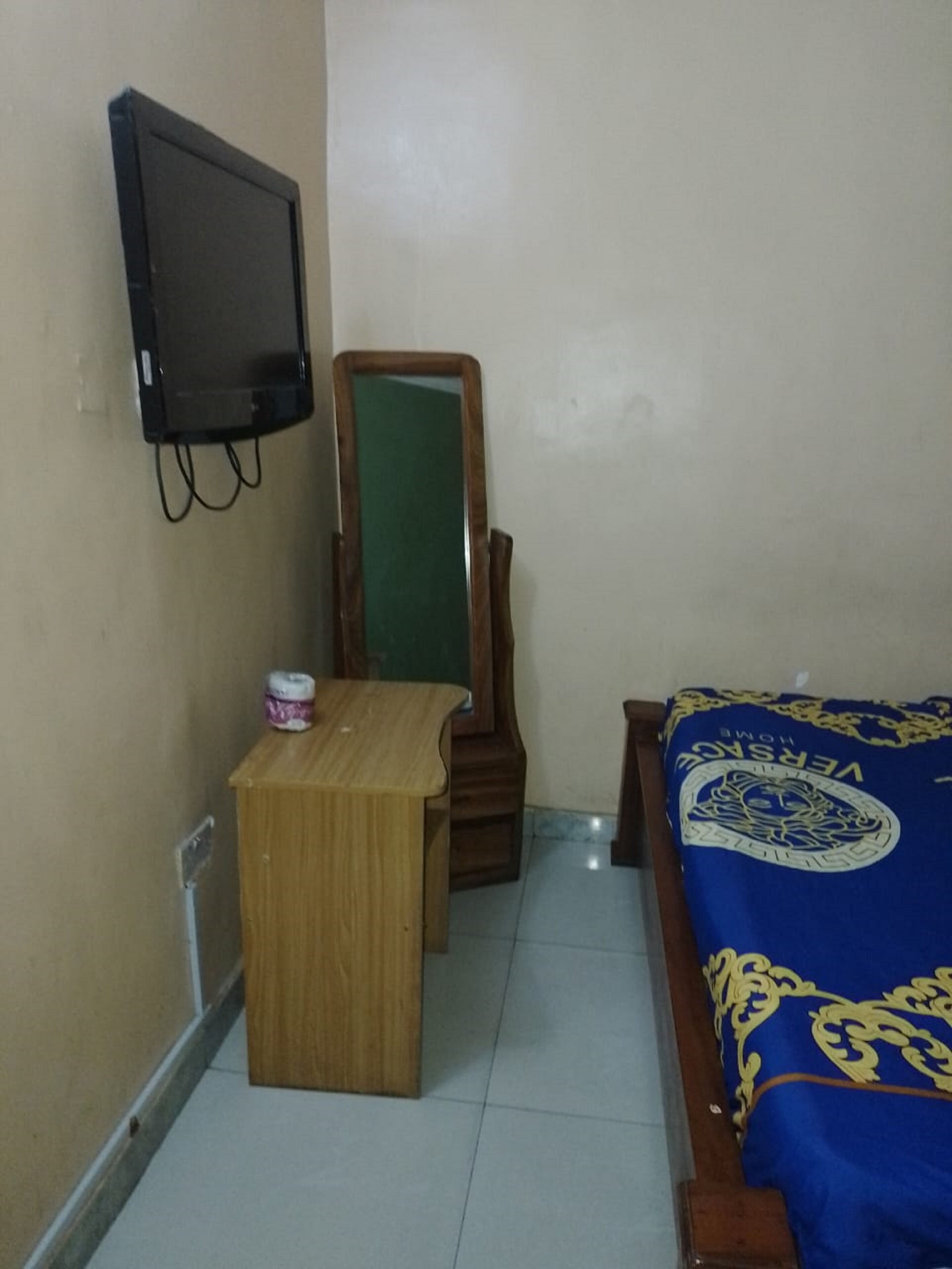 A small room with a bed, a wooden nightstand, a mirror, and a television mounted on the wall.