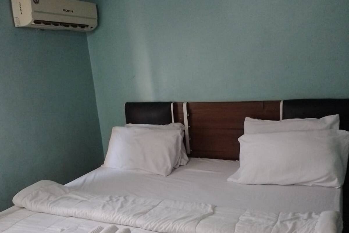 A bed with white bedding, a wooden headboard, and a wall-mounted air conditioner.