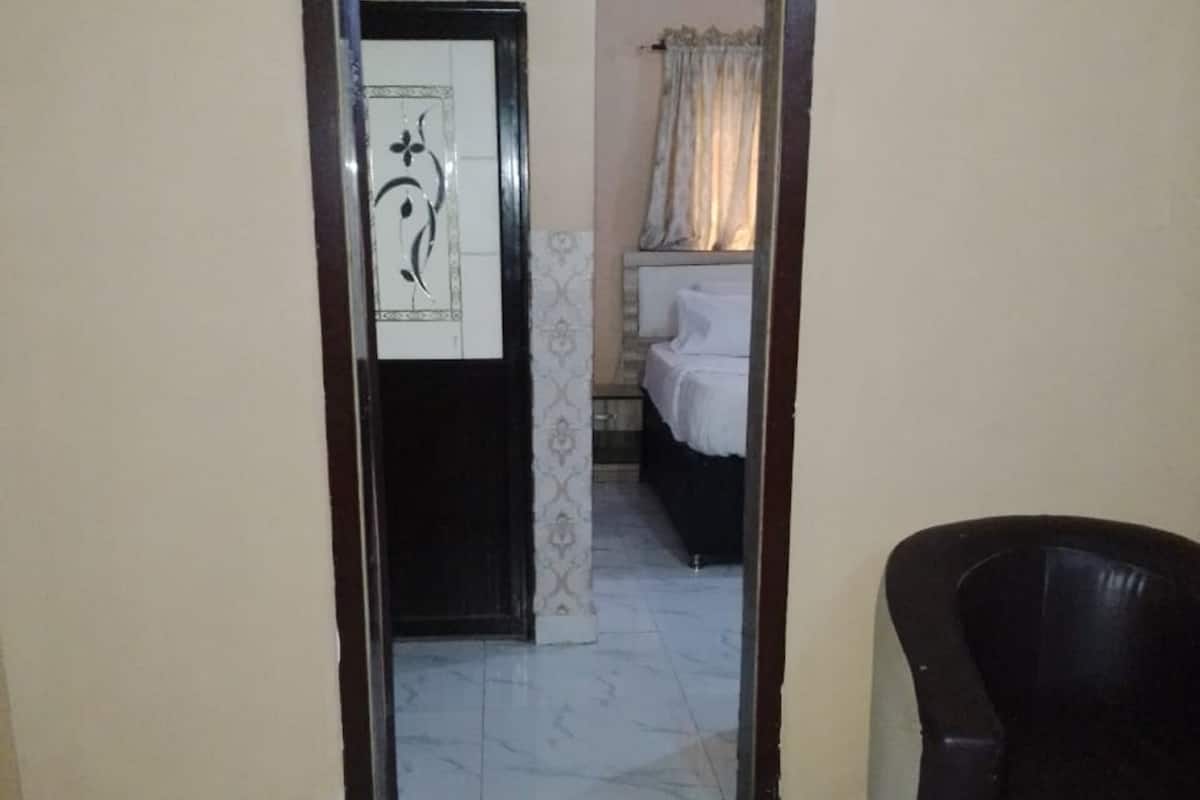 A hallway with a marble floor leading to a bedroom with a bed and a nightstand. A black leather chair is visible in the foreground.
