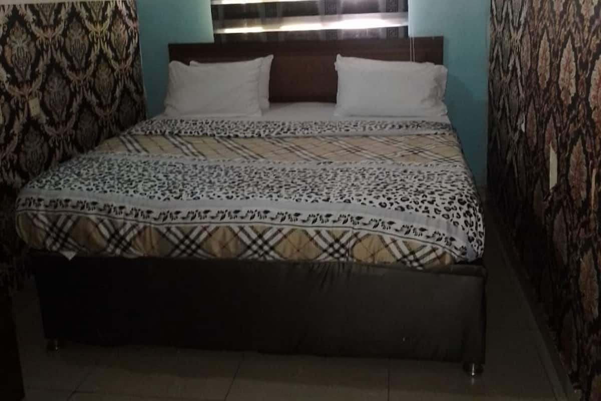 A bedroom with a bed, a window with blinds, and an air conditioning unit on the wall.