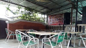 A covered outdoor dining area with metal tables and chairs, a brick wall, and a menu board. - Cynergy Suites Apapa (Lagos)