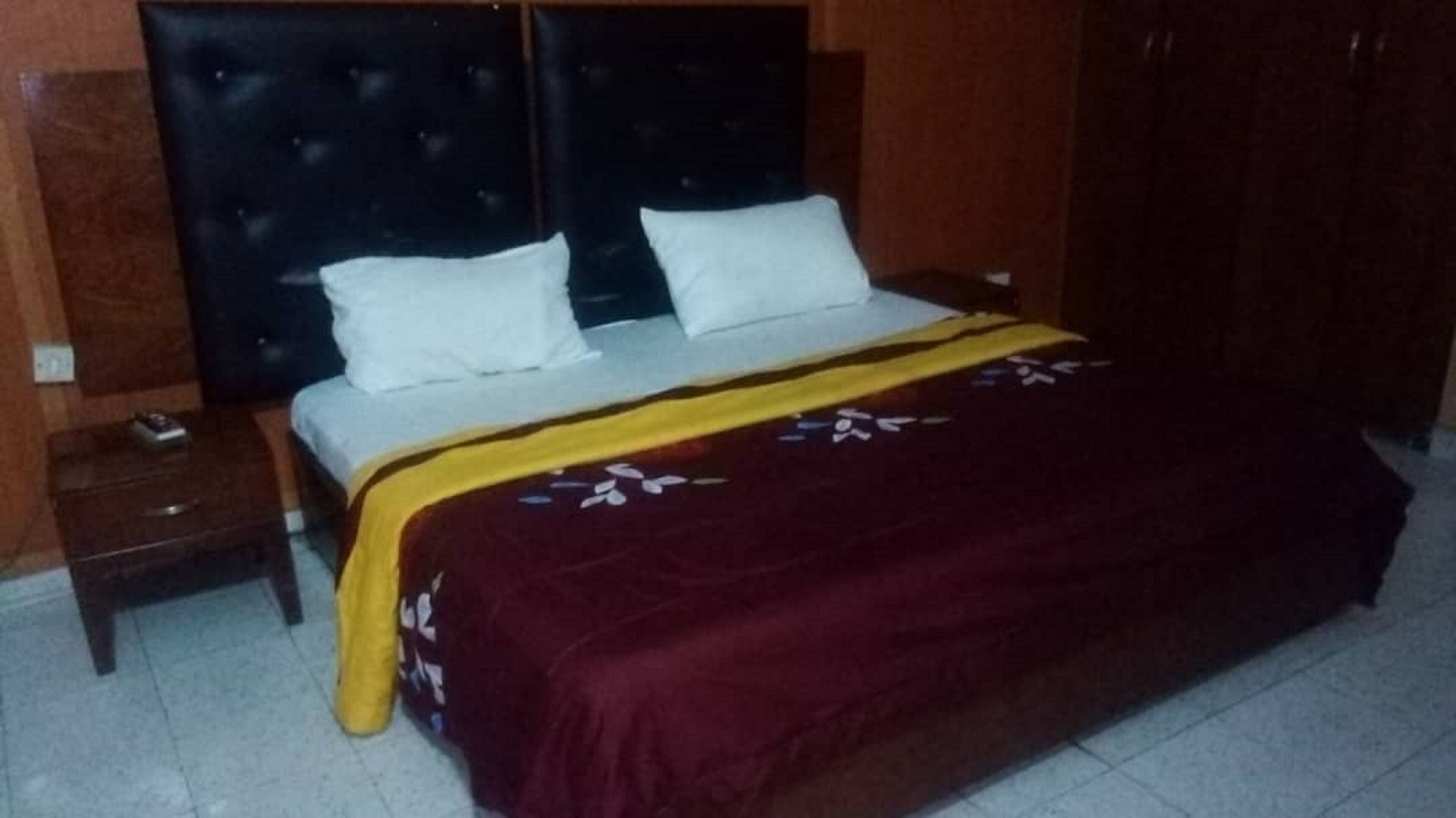 Una habitación de hotel estándar con una cama, una mesita de noche y un cabecero de madera.