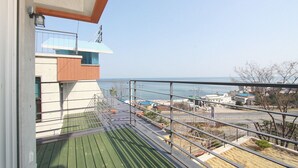 Een balkon met uitzicht op zee, een metalen hek en een gebouw op de achtergrond.