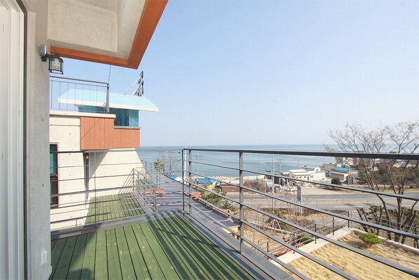 A balcony with a view of the sea, a metal railing, and a building in the background.