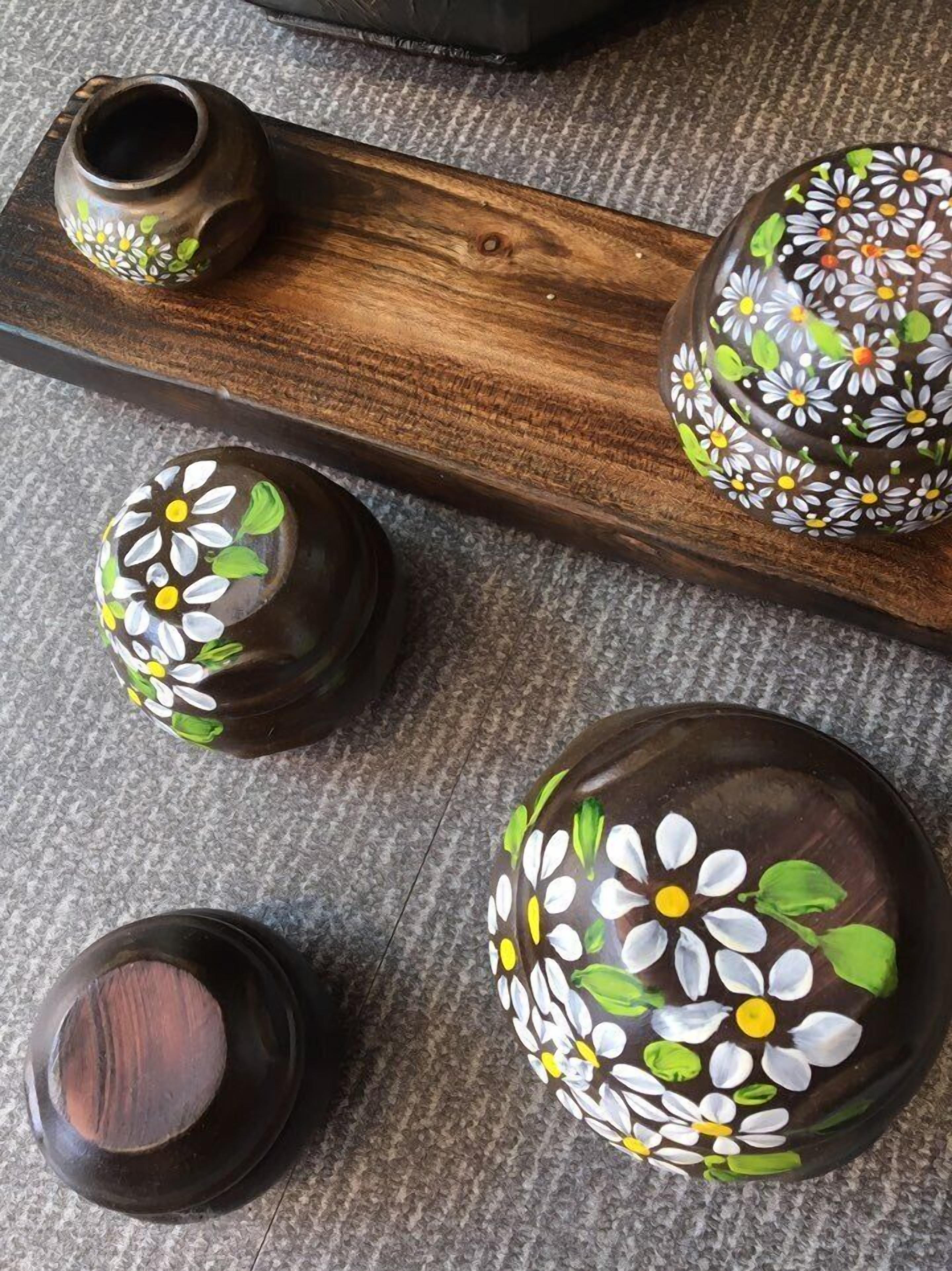 Four ceramic vases with floral designs on a wooden tray.
