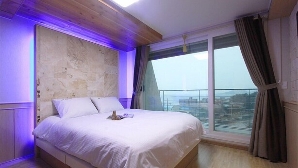 Een slaapkamer met een groot bed, een accentmuur van steen, uitzicht op de stad en een balkon met gordijnen.