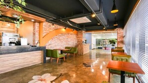 Een modern café met een bakstenen muur, groene zitplaatsen en een keukenhoek.